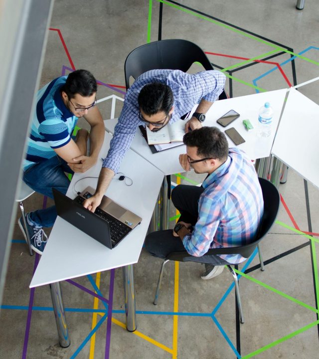 Three men collaborating over a laptop in a modern, geometric-themed office space.